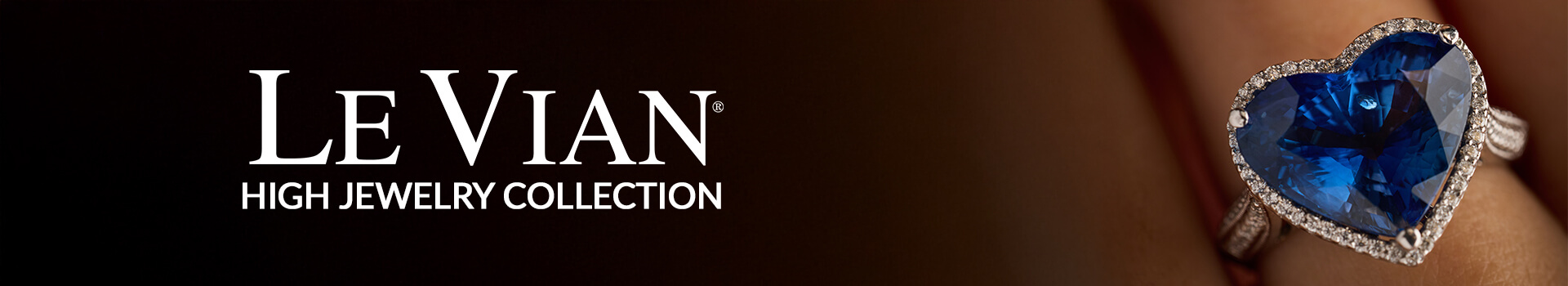 Le Vian® High Jewelry Collection banner with white serif logo text, featuring a close-up of a heart-shaped deep blue sapphire gemstone ring surrounded by a halo of diamonds worn on a model''s hand.