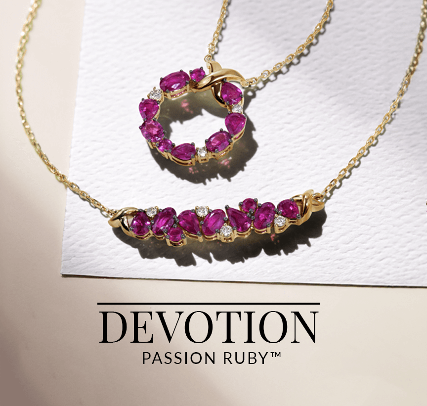 Two ruby and diamond necklaces—one in a heart motif and the other in a bar design—set in yellow gold and displayed on romantic stationery, from Le Vian’s Devotion Passion Ruby™ collection.