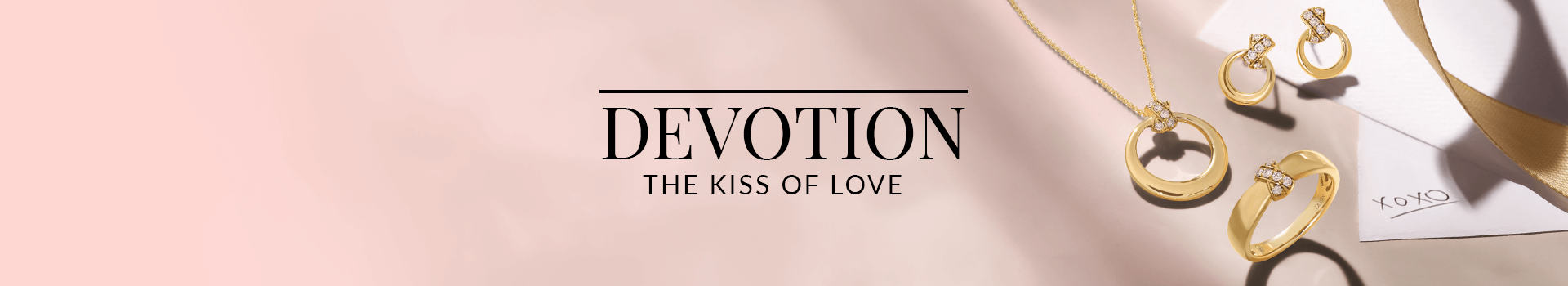 Gold jewelry set including hoop earrings, a ring, and a circular pendant necklace accented with diamonds, arranged beside a romantic note and ribbon, from Le Vian’s Devotion: The Kiss of Love collection.