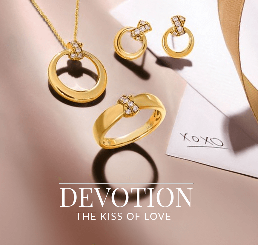 Gold jewelry set including hoop earrings, a ring, and a circular pendant necklace accented with diamonds, arranged beside a romantic note and ribbon, from Le Vian’s Devotion: The Kiss of Love collection.