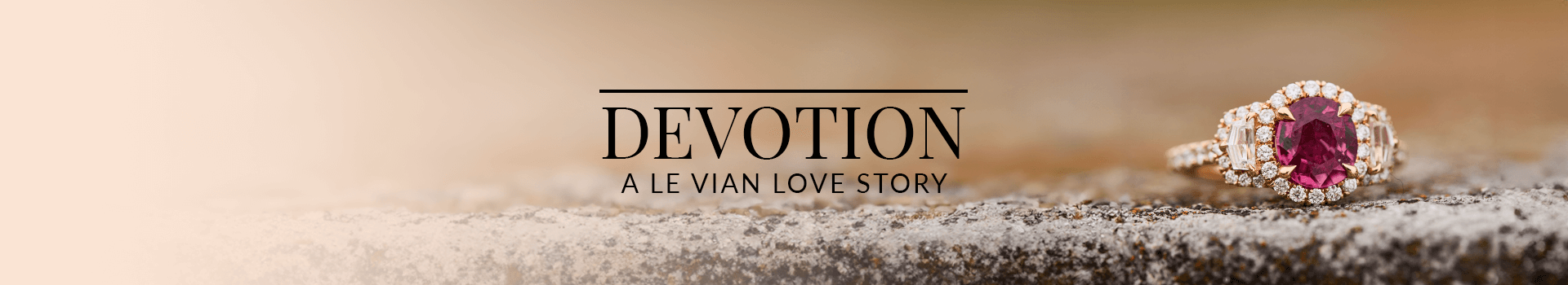 Elegant engagement ring with a ruby gemstone center, flanked by baguette diamonds and a diamond halo, placed on a textured stone surface, from Le Vian’s Devotion: A Le Vian Love Story collection.