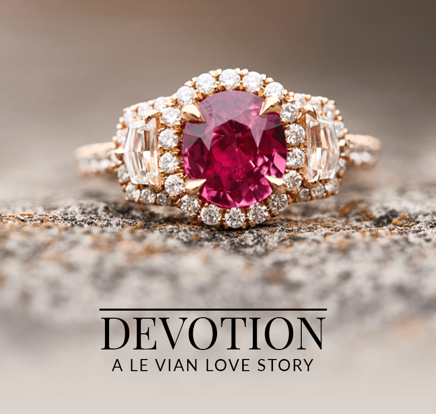 Elegant engagement ring with a ruby gemstone center, flanked by baguette diamonds and a diamond halo, placed on a textured stone surface, from Le Vian’s Devotion: A Le Vian Love Story collection.