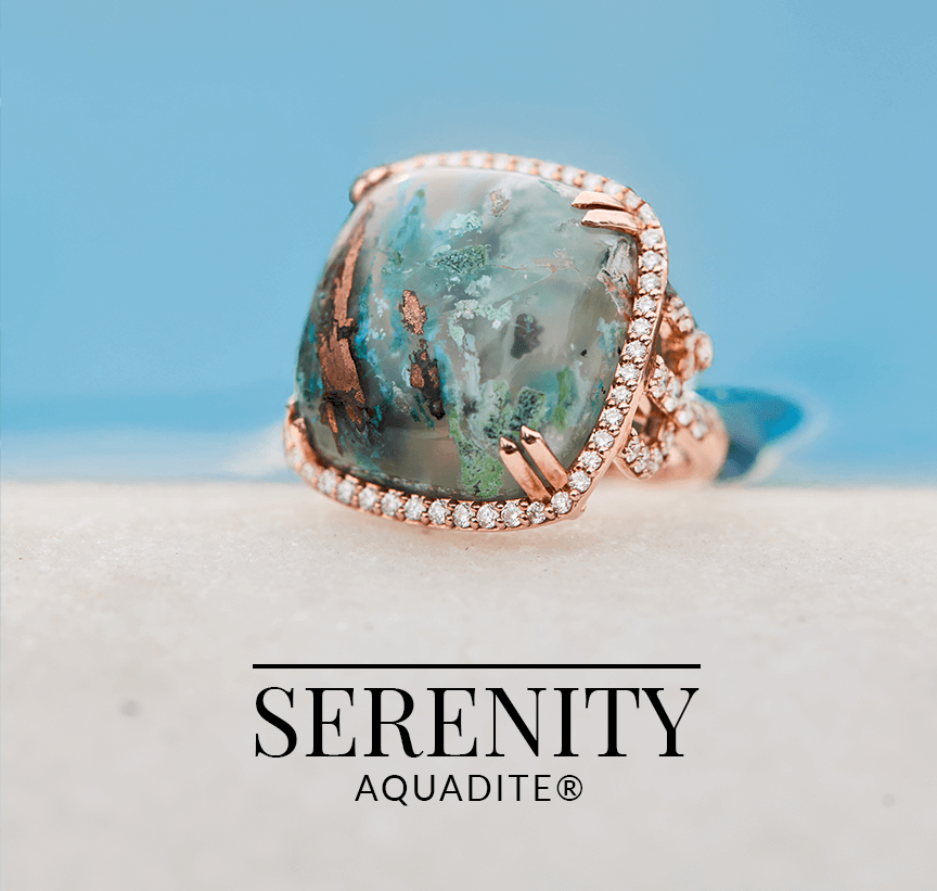 Aquadite® gemstone ring in rose gold and diamond setting, showcasing a marbled oceanic pattern, resting against a serene blue backdrop.