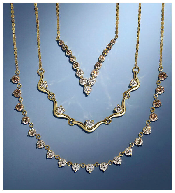 Layered gold necklaces with white and champagne-toned diamonds arranged on a cool blue background, including heart, floral and station designs.