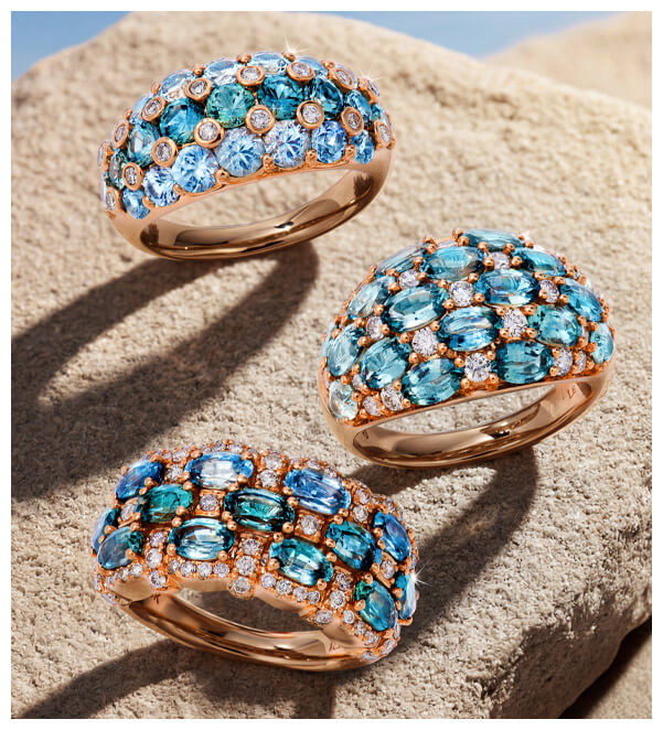 Three rose gold rings with blue-green Montana Sapphire Ombr&eacute; gemstones and white diamond accents, photographed on textured stone.